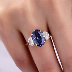 a woman's hand holding a ring with an oval blue sapphire and two white diamonds