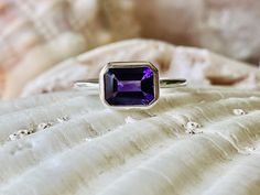 This classic east west bezel setting contains a beautiful 2.00 ct. genuine emerald cut amethyst. The emerald cut stone measures approximately 8x6mm. The ring is available in a satin or high polish finish. The ring is available in sterling silver, and 14k white, yellow, or rose gold. Amethyst is the birthstone for February. Please send me a message if you need a size not listed. * This ring can be customized with any color center stone. All items are handmade by me in my shop in Woodbridge, NJ. P Classic Emerald Cut Solitaire Amethyst Ring, Classic Purple Amethyst Ring With Bezel Setting, Classic Amethyst Ring With Bezel Setting, Classic Amethyst Rings With Bezel Setting, Classic Octagon Amethyst Ring As Gift, Classic Octagon Amethyst Ring For Gift, Classic Octagon Amethyst Ring As A Gift, Classic Amethyst Promise Ring With Bezel Setting, Classic Amethyst Ring With Bezel Setting For Promise