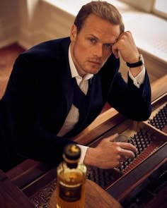 a man in a tuxedo sitting at a piano with a bottle of whiskey