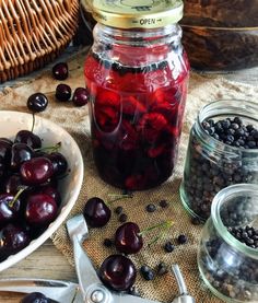 cherries in jars and spoons on a table next to some other fruit items