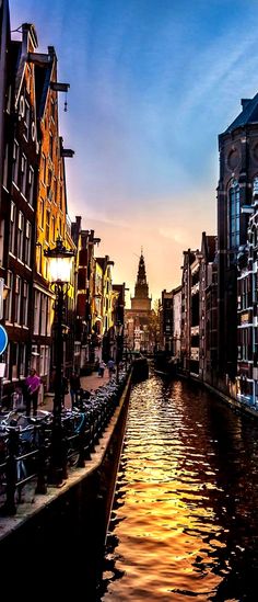 the sun is setting over a canal in an old european city with many buildings and people walking along it