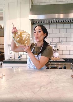 a woman is holding a bowl with food in it while standing at the kitchen counter