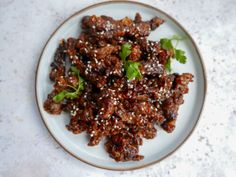 a white plate topped with meat covered in sesame seeds and garnished with cilantro