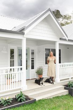 a woman standing in front of a white house with her two dogs on the porch