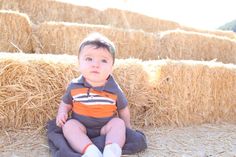 a baby sitting on the ground in front of hay bales