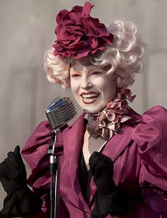 a woman with blonde hair wearing a pink outfit and holding a microphone in front of her