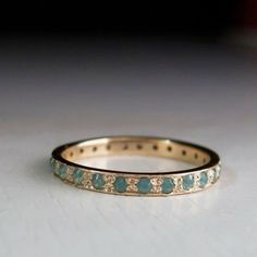 a close up of a wedding ring on a white surface with blue and green stones