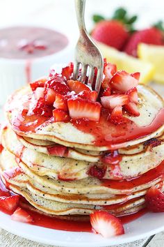 a stack of pancakes covered in strawberries and syrup