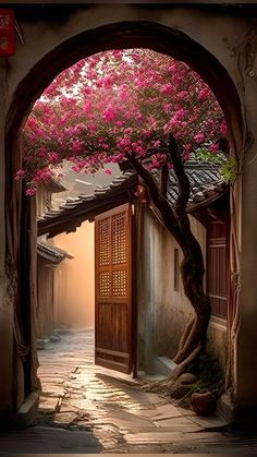 an archway leading into a courtyard with pink flowers on the trees and in the doorway is a door