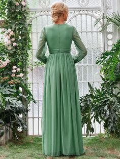 a woman in a green dress looking out into the distance, with flowers and greenery behind her