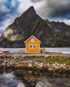 an orange house sitting on top of a rocky shore next to a body of water