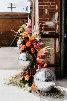 two disco ball vases with flowers and feathers on the ground next to a brick wall