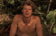 a shirtless man sitting in the woods with his mouth open and eyes wide open