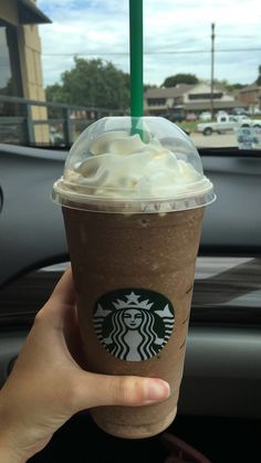 a person holding up a starbucks drink in their hand with a green straw sticking out of it