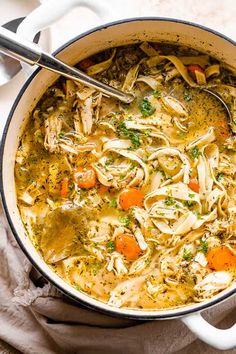 a pot filled with chicken noodle soup on top of a white cloth next to a spoon