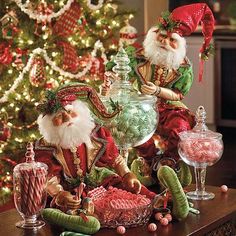 two santa claus figurines sitting on top of a table next to a christmas tree