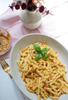 a white plate topped with pasta next to a bowl of sauce