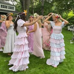 several women in dresses are dancing together on the grass with their hands behind their heads