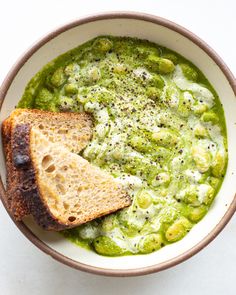 a white bowl filled with green soup and two slices of bread