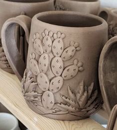 several clay cups and spoons are sitting on a shelf with other pottery items in the background