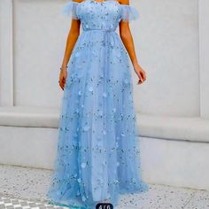 a woman wearing a blue dress standing in front of a white wall with flowers on it