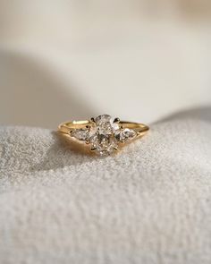 a three stone diamond ring sitting on top of a white cloth covered cushioned surface