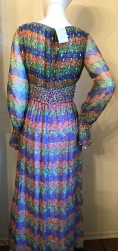 "This is a gorgeous vintage 1970's bohemian dress. It is a colorful peacock feather print polyester chiffon accented with sequins and beading in a peasant style dress. The bodice is smocked and has a scoop neck wide beaded corset style waist with beaded tie bow and sheer sleeves with smocked ruffle cuffs, The skirt is fully gathered and is lined. It has a full nylon zipper up the back. It is in good condition...there may be a few loose sequins, and smocking at cuffs is a little stretched. Priced Multicolor Sequined Maxi Dress, Spring Multicolor Sequined Maxi Dress, Bohemian Sequined Maxi Dress For Evenings, 1970s Style Multicolor Party Dresses, Bohemian Floor-length Sequined Maxi Dress, Peacock Feather Print, Beaded Corset, Beaded Tie, Peasant Style Dress