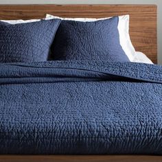 the bed is made with blue quilts and pillows on top of it, next to a night stand