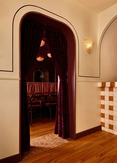 an arched doorway leading to a dining room with wooden floors and red drapes on the curtains