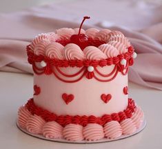 a pink cake decorated with hearts and a cherry sitting on top of a white table