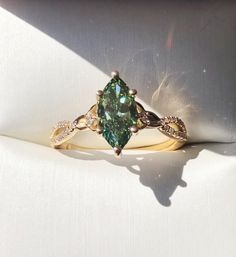 a fancy ring with a green stone surrounded by white and yellow gold accents on a white cloth