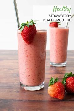 two glasses filled with strawberry peach smoothie on top of a wooden table next to strawberries