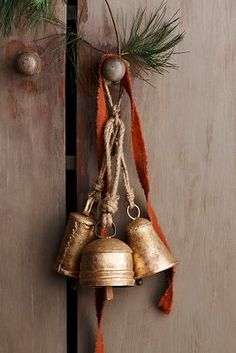 two bells hanging from the side of a wooden door next to pine needles and twine