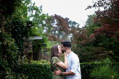 a man and woman kissing in front of some bushes