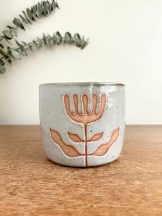 a white and orange bowl sitting on top of a wooden table next to a plant