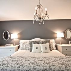 a white bed sitting in a bedroom next to two nightstands and a chandelier