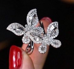 a woman's hand holding a diamond ring with leaves on the top and bottom