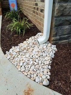 a white pipe sticking out of the ground next to a brick wall and flower bed