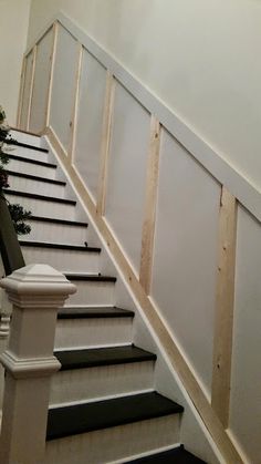 a white staircase with black steps and christmas tree on the bottom handrail, next to an unfinished wall