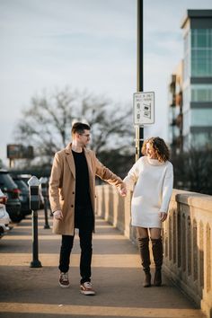 a man and woman holding hands while standing on a bridge next to each other with cars in the background