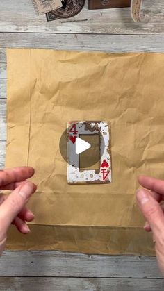 two hands holding up a piece of brown paper with an image of playing cards on it