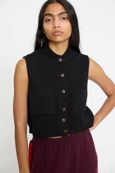 A chunky knit vest in a black cotton blend. Features a bomber collar, contrast button closure, and two front pockets. Color: Black Material: 80% Ecotec Cotton, 20% Ecotec Polyester Relaxed fit Measures appoximately: 15" W x 19" L Made in Spain Anugraha is 5'8". This item is one size only. Chunky Knit Vest, Denim Short Jumpsuit, Icon Clothing, Textile Wall Hangings, Icon Shoes, Iconic Dresses, Short Jumpsuit, Denim Jumpsuit, Knit Vest