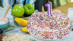 a birthday cake with white frosting and sprinkles sits on a table