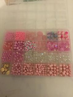 a plastic container filled with lots of pink and white beads next to a gold coin