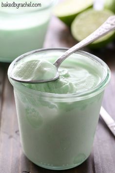 a spoon in a jar filled with yogurt next to cucumber slices