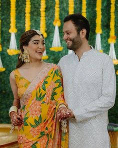 a man and woman standing next to each other in front of yellow flowers on the wall