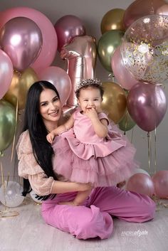 a woman holding a baby girl in front of balloons and streamers on the wall