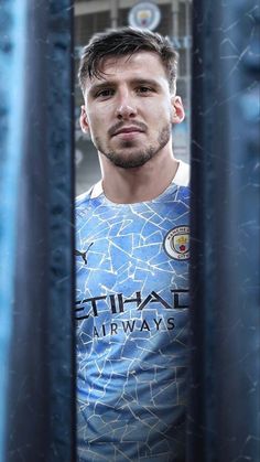 a man standing in front of a metal fence wearing a blue shirt and looking at the camera