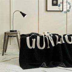 a black blanket with the word u on it sitting next to a chair and lamp