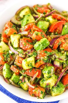 a white bowl filled with lots of veggies on top of a blue and white table cloth